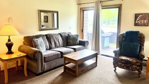 A living room with a sofa, coffee table, armchair, lamp, and a mirror on the wall. - Cozy 2 Bed, 2 Bath Condo on Golf Course with Hot tub, Sauna & Pool! (Red Lodge)