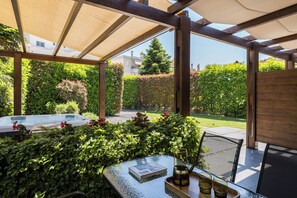 A covered patio with a glass table, chairs, a hot tub, and lush greenery. - Meteora boutique villa A (Kalampaka)