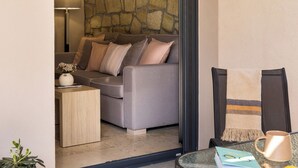 A modern living room with a stone accent wall, a sofa with cushions, a small side table, and a glass table with a book and mug. - Meteora boutique villa A (Kalampaka)