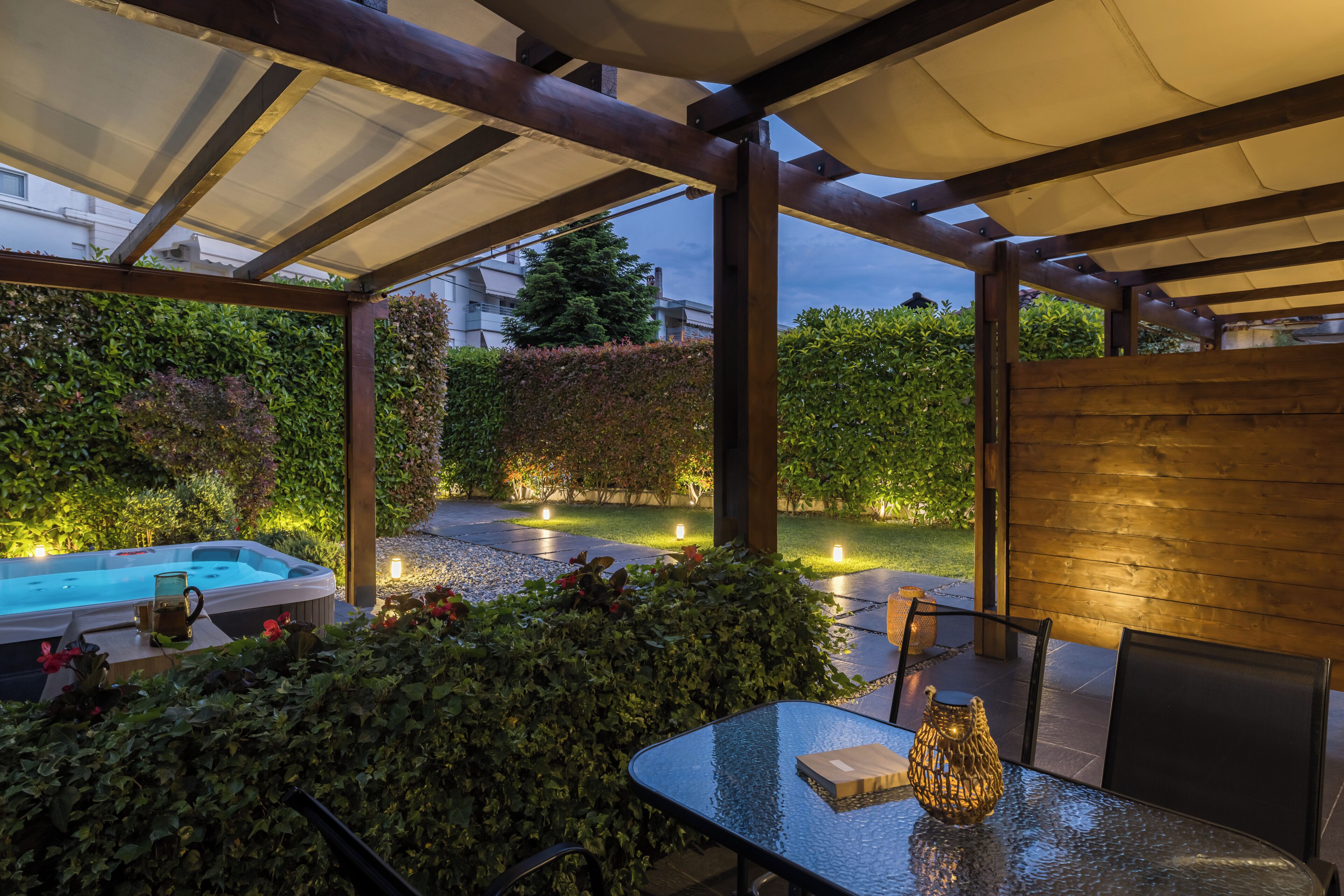 Een terras buiten met een glazen tafel, stoelen, een jacuzzi en een houten hek.