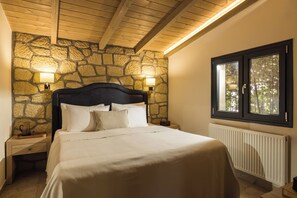 A bedroom with a stone wall, a wooden ceiling, a bed with white bedding, two bedside lamps, and a window with a view of trees. - Meteora boutique villa A (Kalampaka)