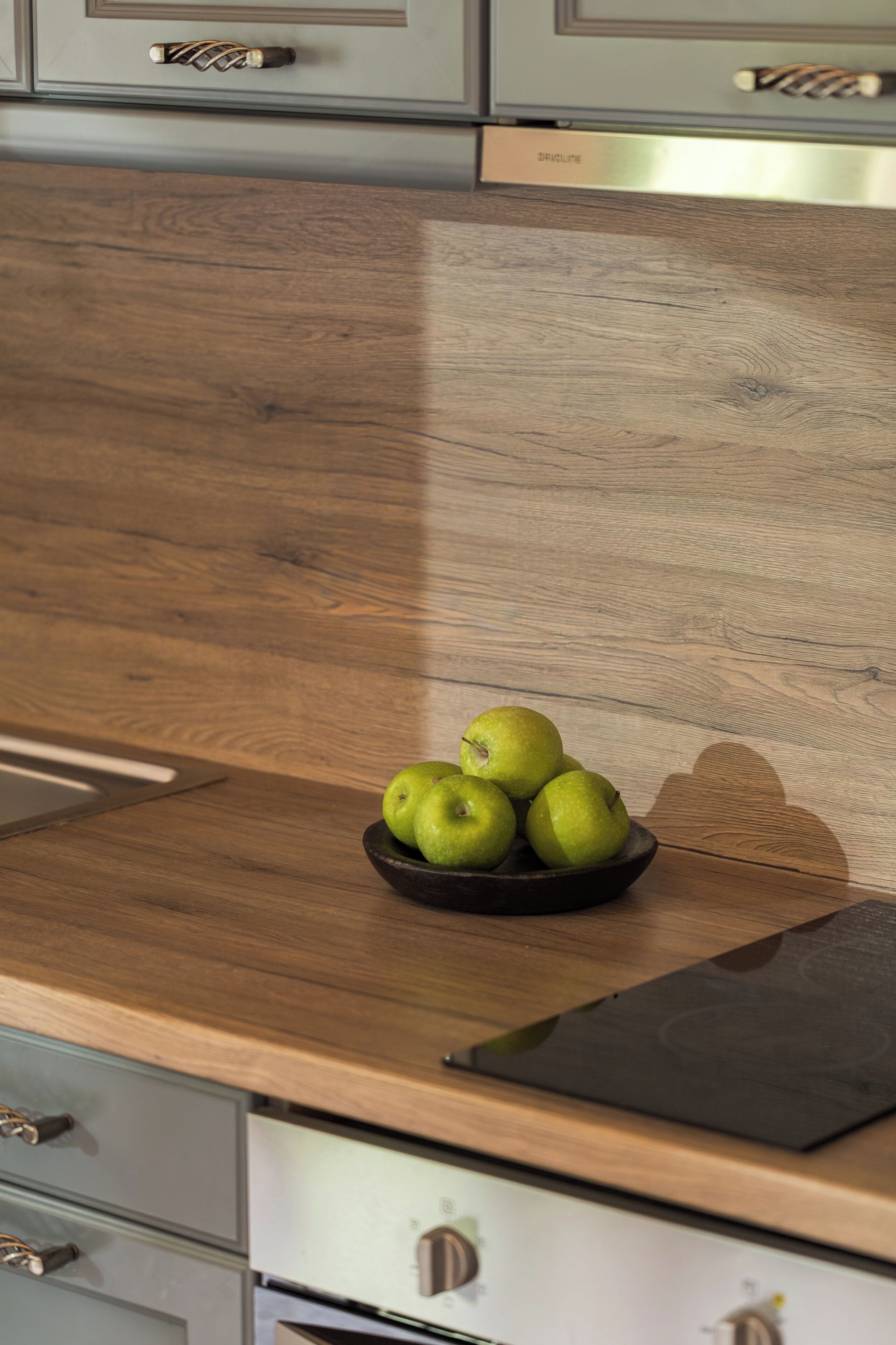 A kitchen with a wooden countertop, a bowl of green apples, and a black cutting board.
