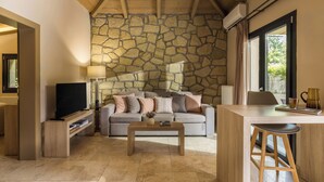 A living room with a stone wall, a sofa, a coffee table, a TV, and a bar area. - Meteora boutique villa A (Kalampaka)