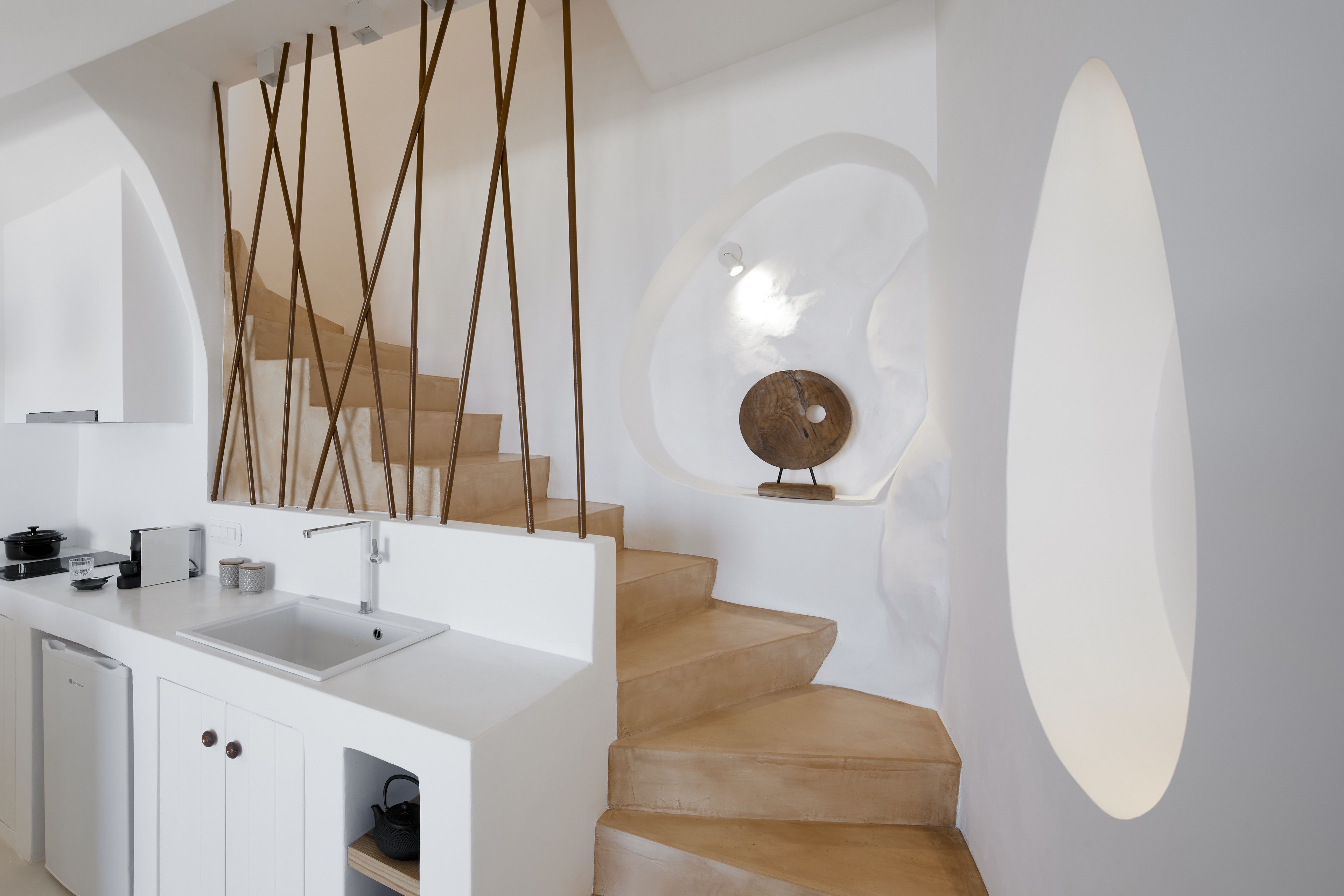 Une cuisine moderne avec un plan de travail blanc, un évier et un escalier en bois doté d’un motif circulaire original sur le mur.