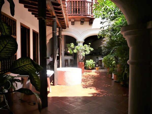 A courtyard with a central white circular structure, surrounded by potted plants and a wooden pergola.