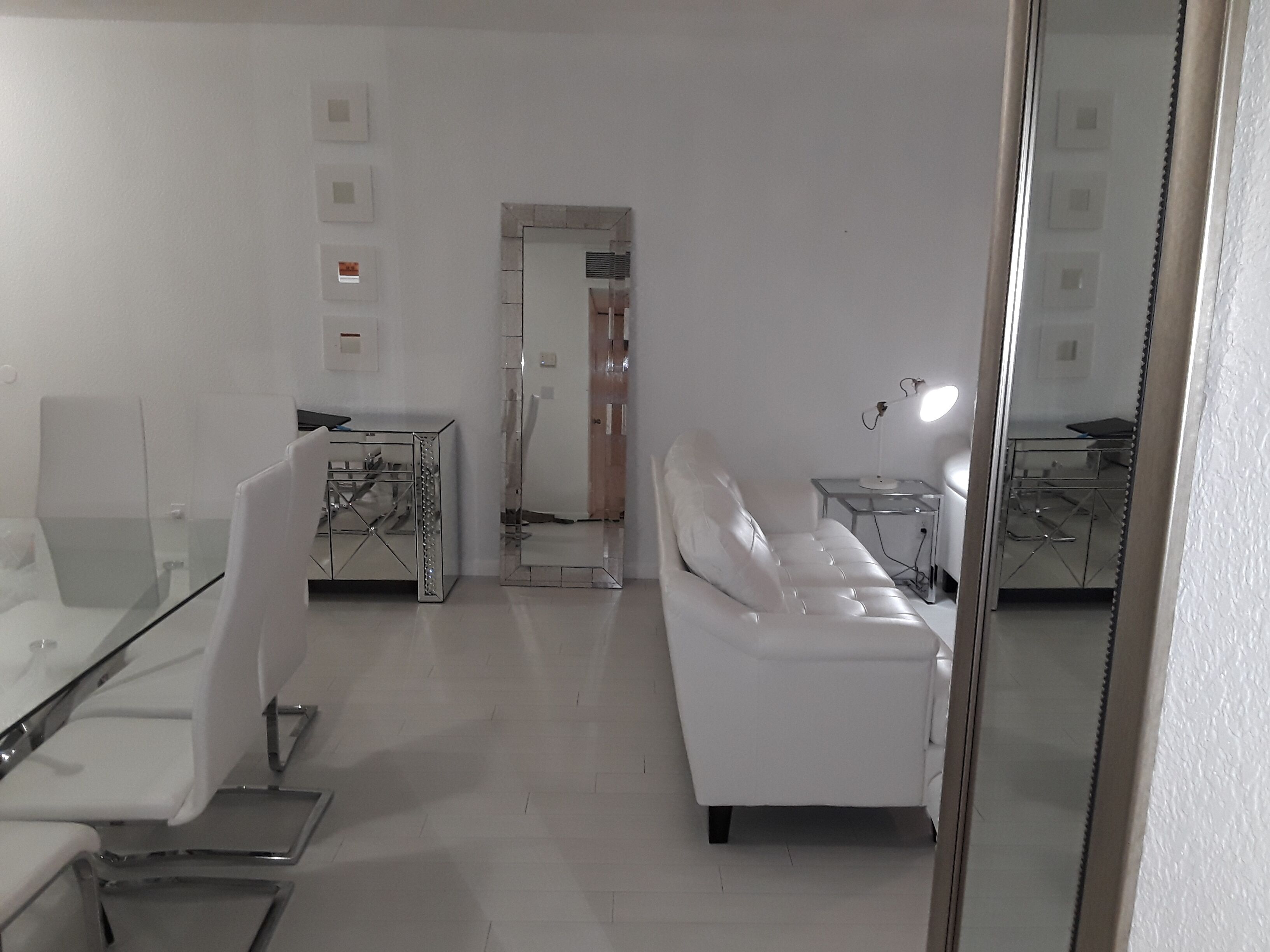 A modern living room with a white sofa, a glass coffee table, and a mirrored cabinet.
