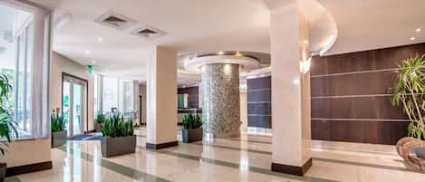 A spacious lobby with a polished floor, large pillars, and potted plants.