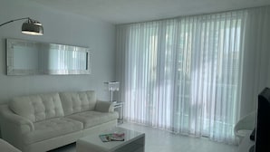 Ein modernes Wohnzimmer mit einem weißen Sofa, einem Glastisch, einer Stehlampe und transparenten Vorhängen.