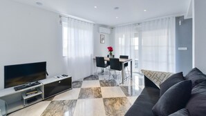 Una sala de estar moderna con una televisión de pantalla plana, un sofá, una mesa de comedor con sillas y una mesa de centro.