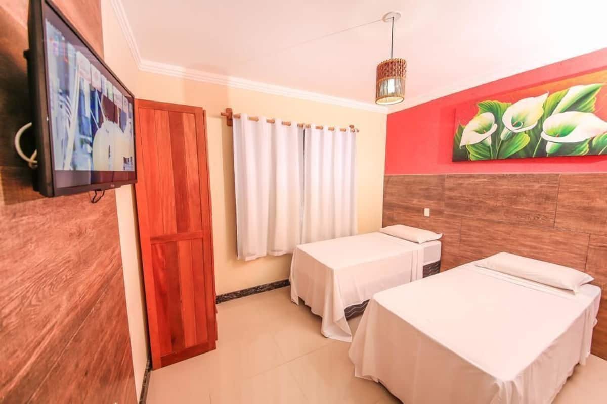 Ein Hotelzimmer mit zwei Betten, einem Fernseher, einer Holztür, einem Vorhang und einem Wandbild.