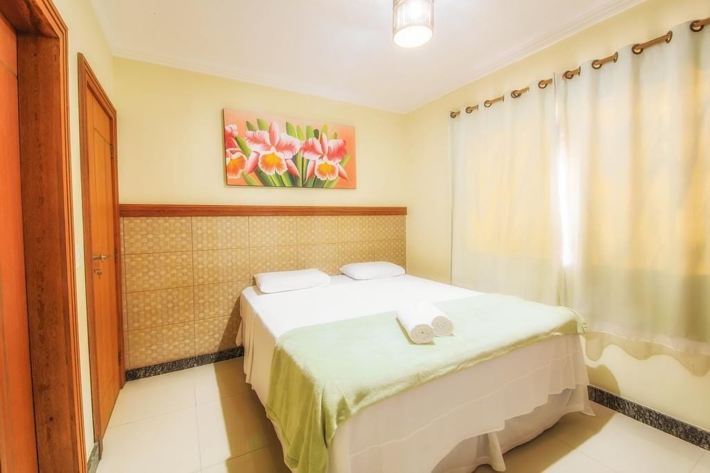 A hotel room with a bed, a painting of flowers on the wall, and a curtain.