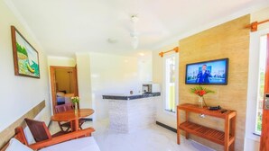 A hotel room with a bed, a wooden table, a TV, and a small kitchen area. - Vila Miola Hotel (Porto Seguro)