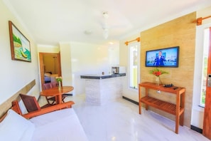 A hotel room with a bed, a wooden table, a TV, and a small kitchen area. - Vila Miola Hotel (Porto Seguro)