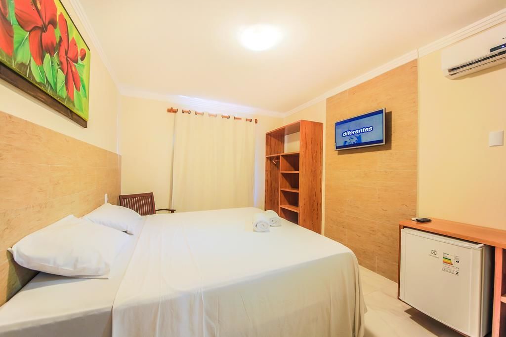 A hotel room with a bed, a TV, a wardrobe, and a desk with a computer.