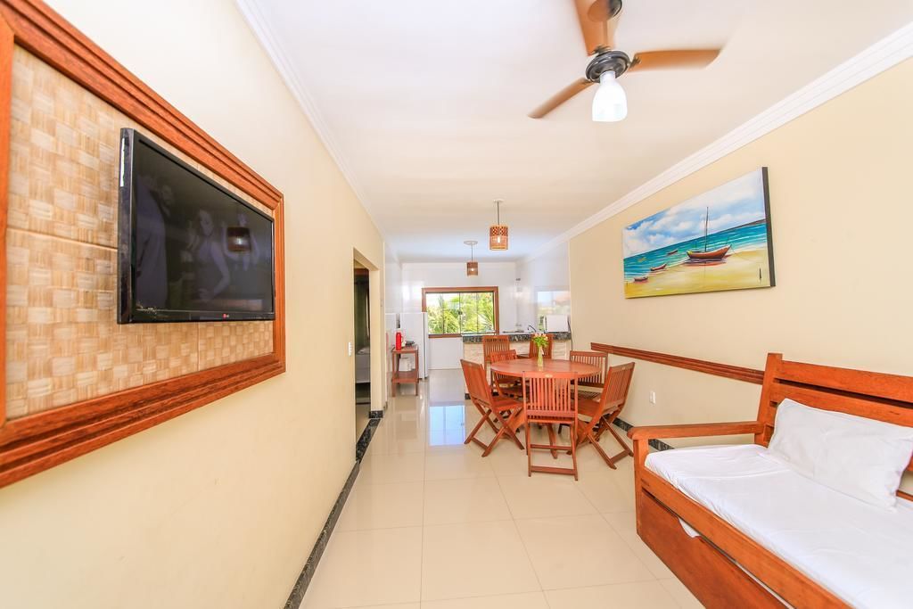 Una habitación con cama, una mesa de comedor con sillas, un televisor montado en la pared y un ventilador de techo.