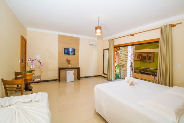 A hotel room with a bed, a desk, a chair, a small fridge, a TV, and a balcony with a view.