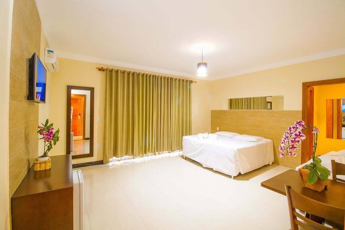 Ein Hotelzimmer mit Bett, Schreibtisch, Stuhl, Fernseher, Spiegel und einem fensterbepflanzten Fenster.