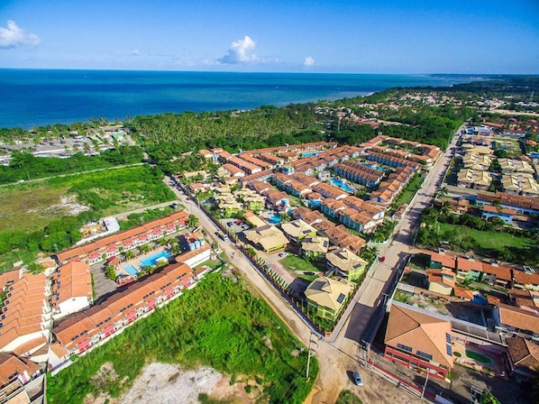 An aerial view of a coastal resort with multiple buildings, a swimming pool, and a view of the ocean. - Vila Miola Hotel (Porto Seguro)