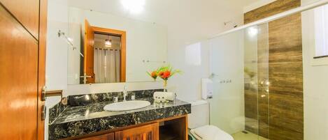Un baño moderno con lavamanos de mármol, tocador de madera y cabina de ducha de vidrio.