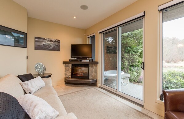 A modern living room with a fireplace, a flat-screen TV, and a large sliding glass door leading to a garden.