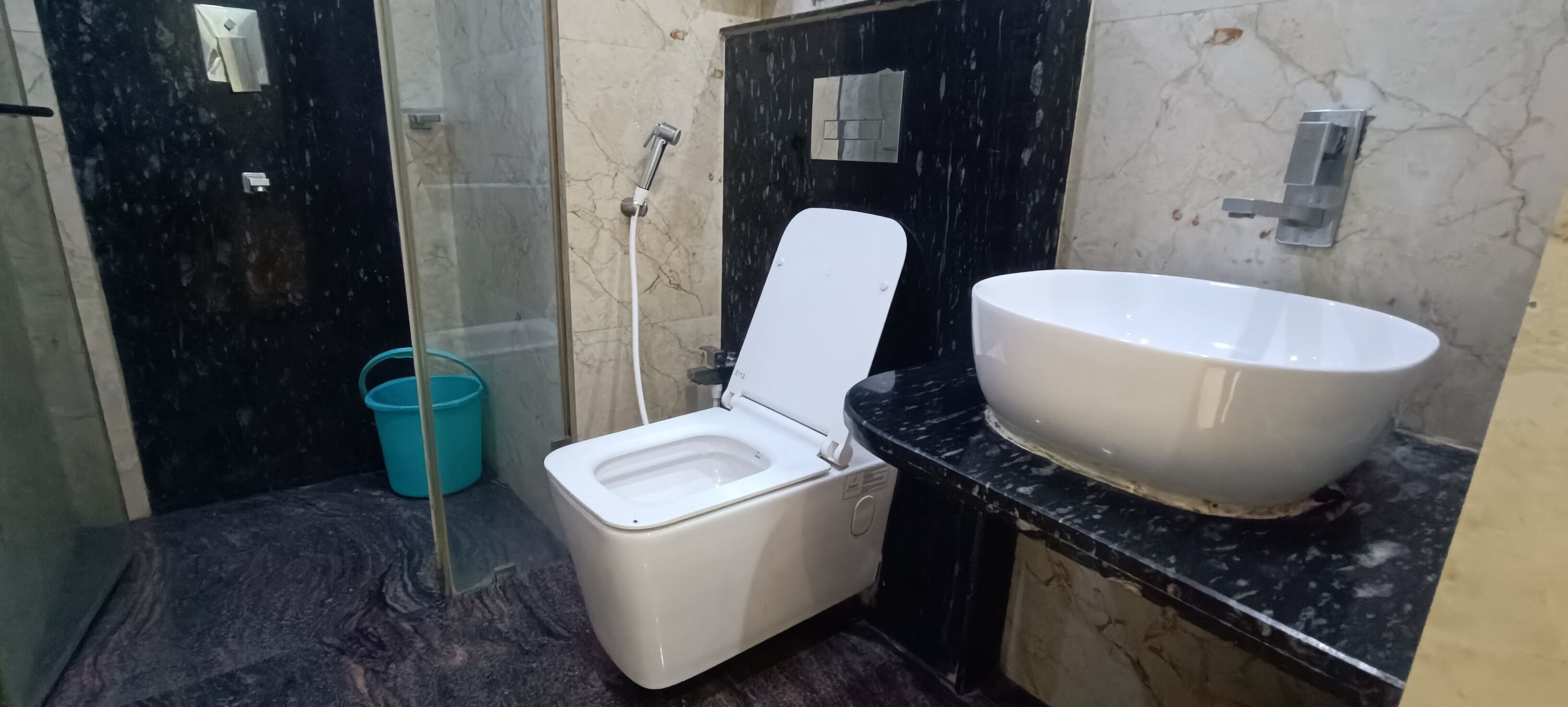 A bathroom with a toilet, a large sink, a shower, and a blue bucket.