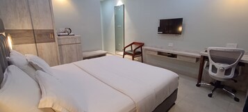 Une chambre d’hôtel avec un lit, un bureau et une chaise, une télévision et une douche.