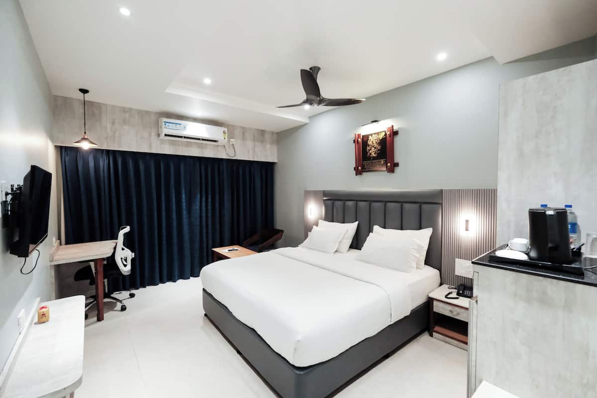 A modern hotel room with a large bed, desk, chair, and a small kitchenette.