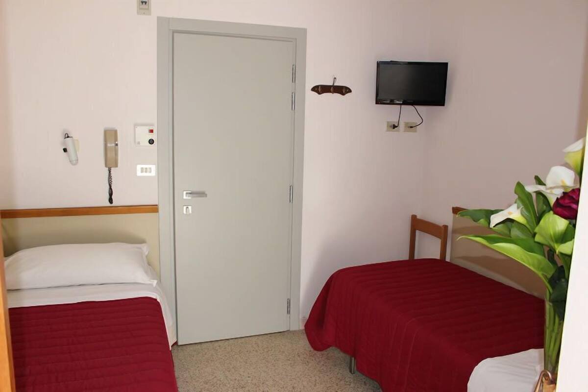 A hotel room with two single beds, a TV mounted on the wall, a door, and a telephone.