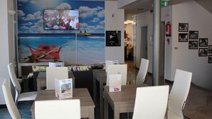 Vestíbulo de hotel con una gran pantalla de televisión mostrando un evento grupal, un mural de un barco en el agua y varias mesas con sillas.
