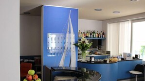 Un área de recepción con un mostrador azul, una decoración con un velero, un frutero y una barra con diversas botellas.