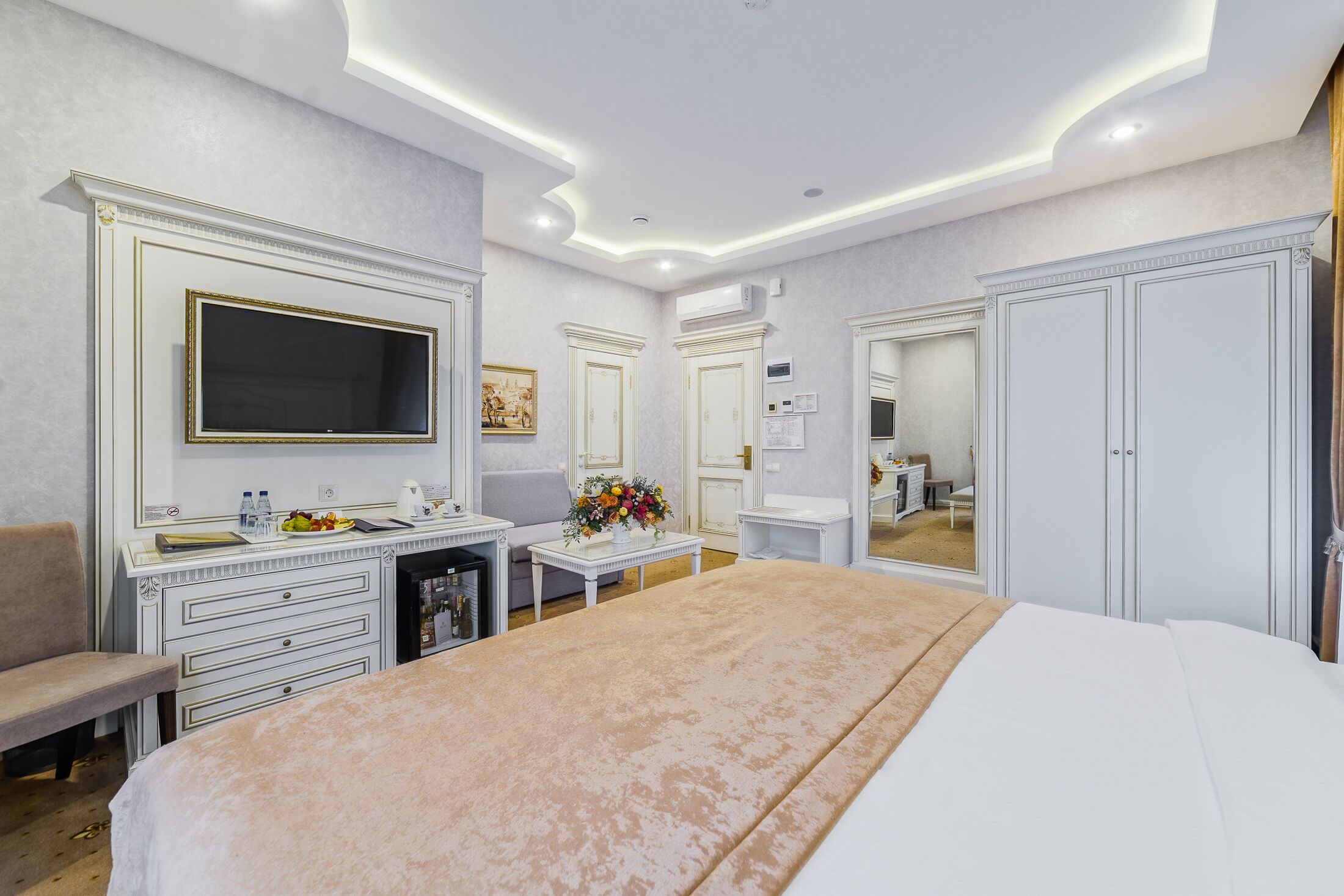 A hotel room with a large bed, a desk with a flat-screen TV, a vanity with a mirror, and a wardrobe.