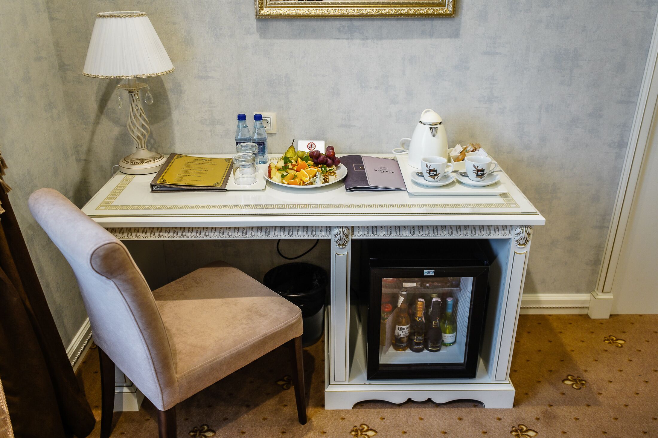 A hotel room with a dining table set for breakfast, including a plate of fruit, a coffee pot, and a menu.