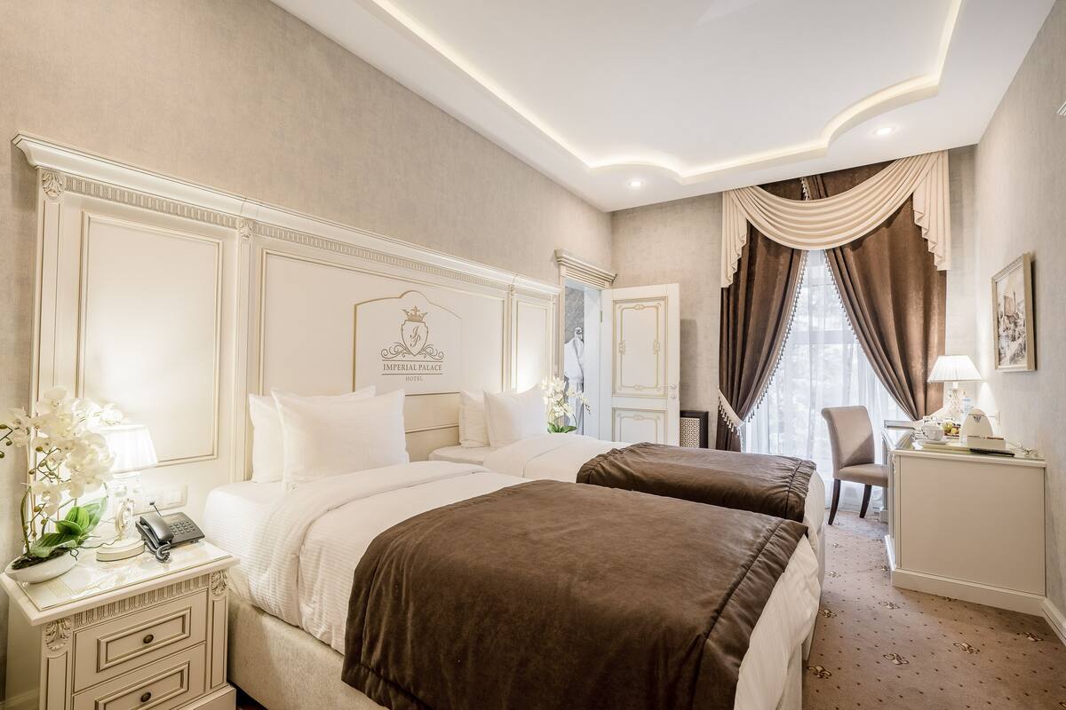 Une chambre d’hôtel avec deux lits, un bureau, une chaise et une grande fenêtre avec des rideaux.