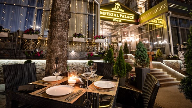 Un espace de restauration en plein air à l’hôtel Imperial Palace, avec des tables pour deux, des bougies et une vue sur l’entrée de l’hôtel.