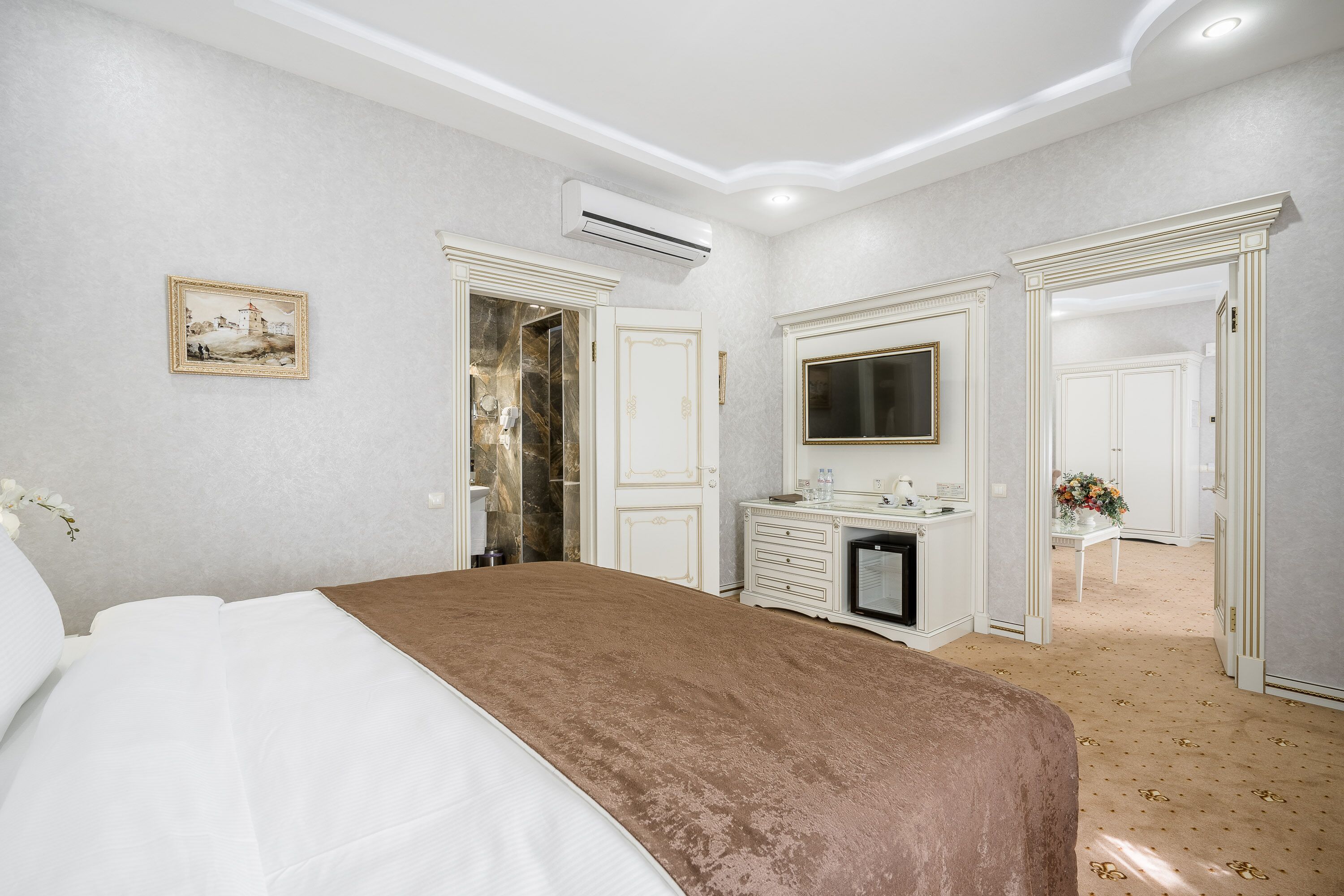 A hotel room with a large bed, a dresser, a vanity, and a television.