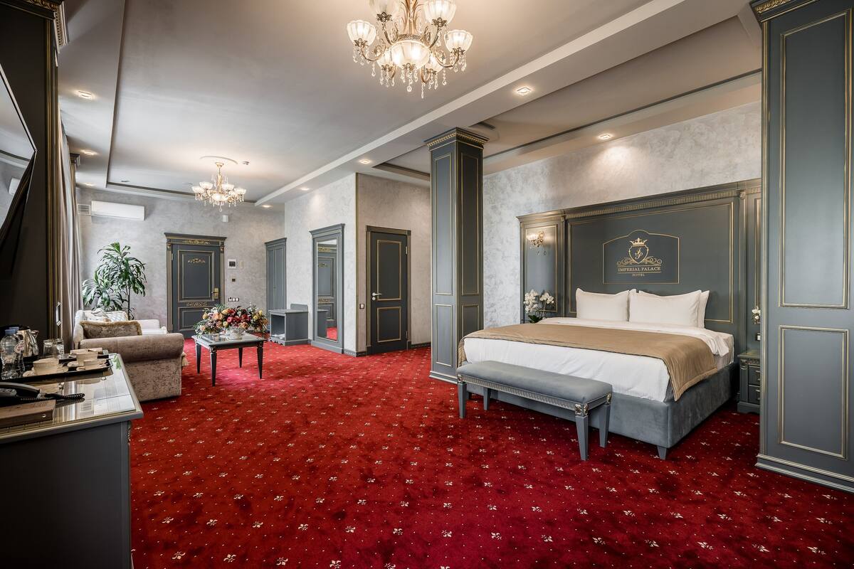Une chambre à coucher luxueuse, dotée d’un grand lit, d’une banquette, d’un bureau et d’un lustre.