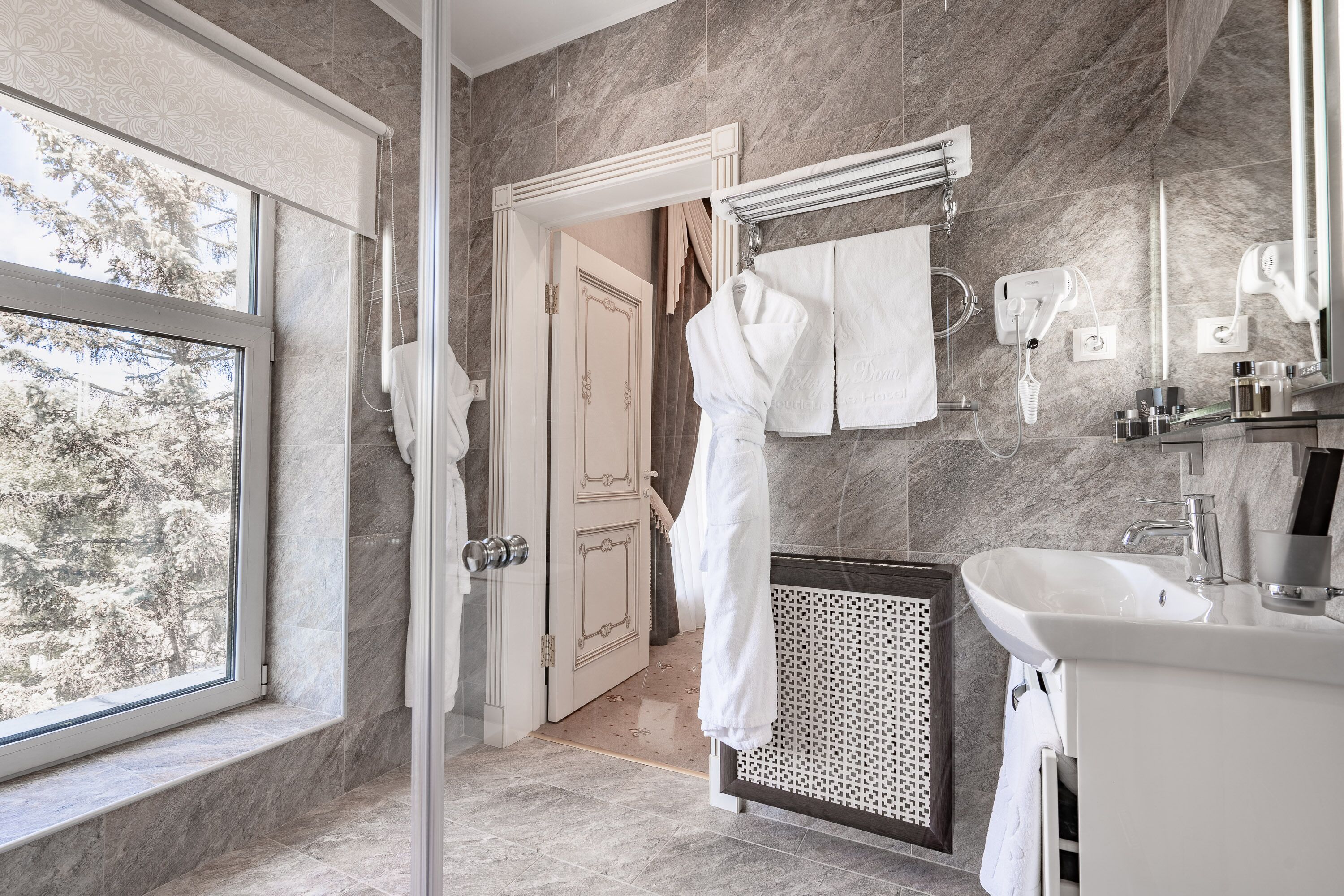 Une salle de bain moderne dotée d’une grande fenêtre, d’une douche à l’italienne, d’un meuble-lavabo et d’un porte-serviettes.