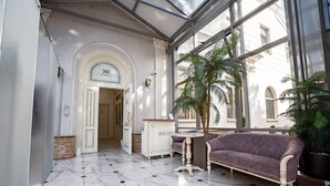 Ein Empfangsbereich mit Marmorboden, einer Rezeption, einem violetten Sofa und einem großen Fenster mit Blick auf die Straße.