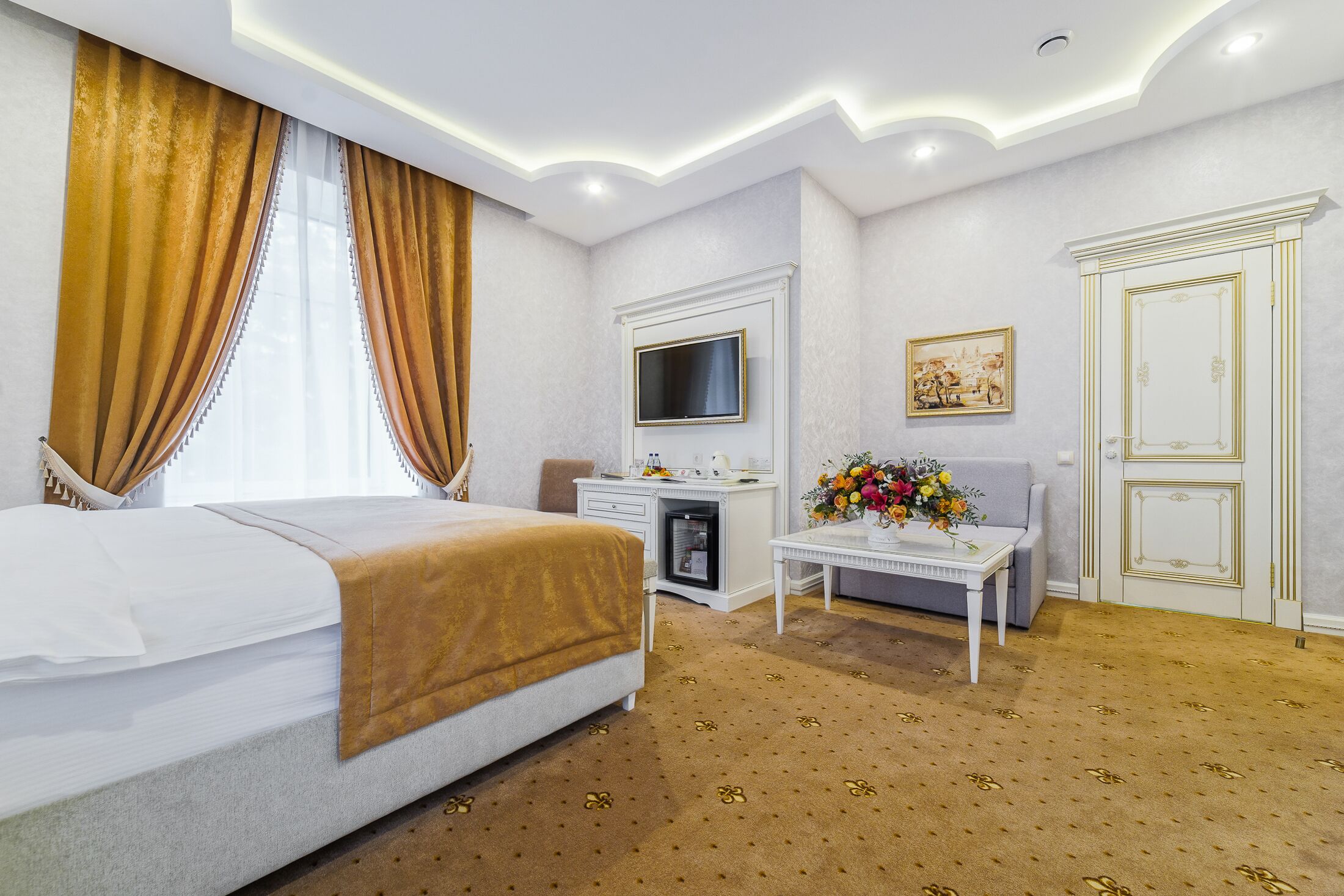 Een hotelkamer met een bed, een bureau, een televisie, een bank en een decoratieve vaas.