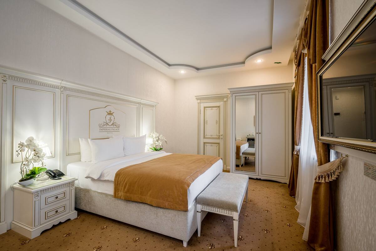 Une chambre à coucher avec un grand lit, des tables de chevet, un banc, un miroir et une armoire.