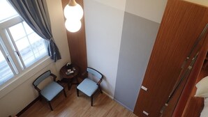 Ein Zimmer mit zwei Stühlen, einem kleinen Tisch, einer Hängelampe, einem Fenster mit Vorhängen und einer Holztür.