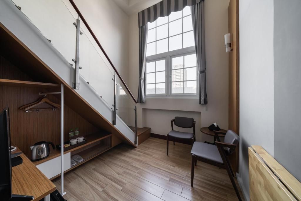 A room with a wooden staircase, a small table with a chair, and a window with curtains.