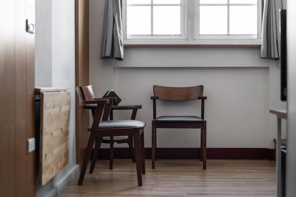 Une pièce avec un plancher en bois, une fenêtre avec des rideaux et deux chaises en bois.