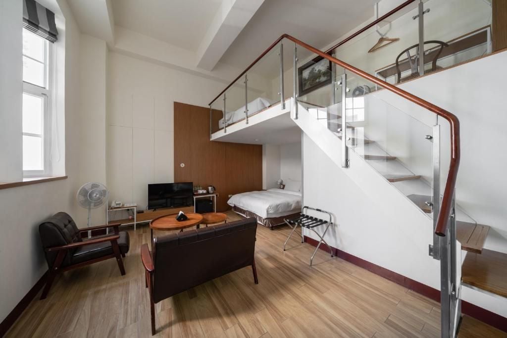 Una moderna camera d'albergo con un letto a soppalco, una TV a schermo piatto, un divano, un tavolo da pranzo e una scala con ringhiere in vetro.
