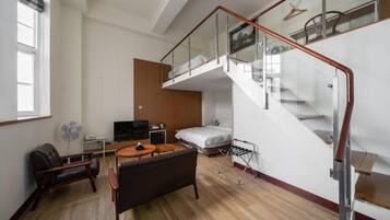 Una moderna camera d'albergo con un letto a soppalco, una TV a schermo piatto, un divano, un tavolo da pranzo e una scala con ringhiere in vetro.