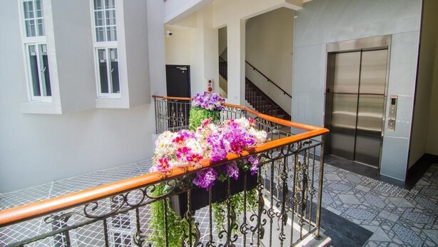 Ein Hotelgang mit Treppe, Aufzug und einem Balkon mit Blumen.