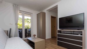 Ein modernes Schlafzimmer mit einem Bett, einem Fernseher auf einem Schrank, einem kleinen Tisch mit einer Vase und einer Schiebetür, die auf einen Balkon führt.