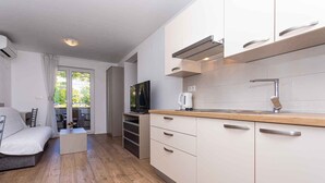 Eine moderne Küche mit weißen Schränken, einer Holzausziehtafel und einem eingebauten Herd. Im angrenzenden Wohnbereich befindet sich eine Couch und ein Couchtisch.