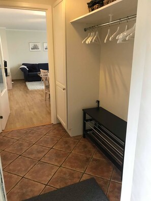 A hallway with a tiled floor, a coat rack with hangers, a bench, and a door leading to another room. - Solferie Barnevennlig & Sentralt (Kristiansand)