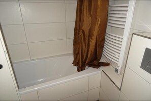 Et badeværelse med et hvidt badekar, et brunt bruseforhæng og en hvid flisevæg.